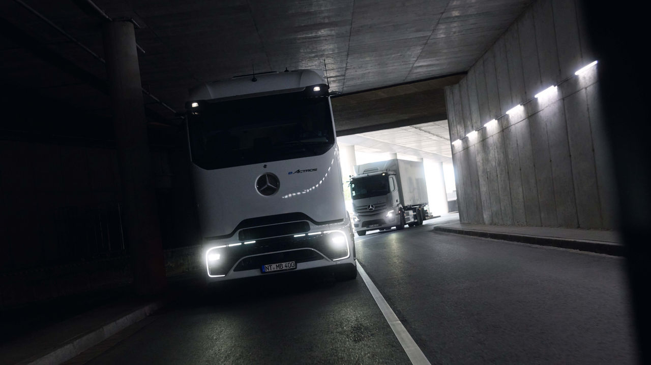 Dva eActros 400, jeden s ProCabin a druhý s osvědčenou kabinou, projíždějí tmavým tunelem s rozsvícenými světlomety. Na konci tunelu je vidět jasné denní světlo, které vytváří kontrast k temnému okolí.